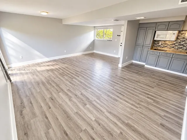 Open-concept area featuring wood-finish flooring, grey cabinetry, mosaic tile backsplash, and a built-in microwave