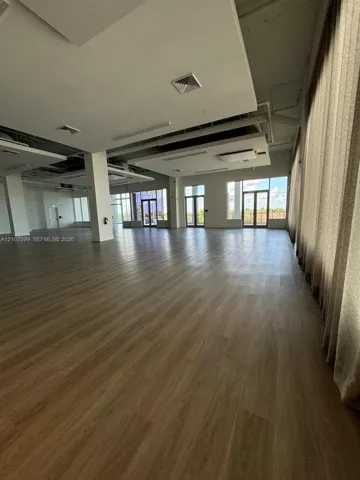 Open-concept interior featuring wood-finish flooring, recessed ceiling architectural elements, multiple glass-paneled entryways, and floor-to-ceiling windows