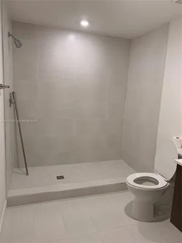 Walk-in shower with floor-to-ceiling textured tile surround, built-in metal shower fixtures, recessed ceiling lighting, and large-format tile flooring