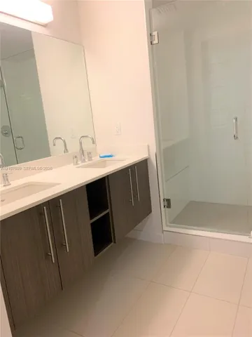 Floating dual-sink vanity with wood-finish cabinetry, solid-surface countertop, and glass-enclosed shower with tiled flooring