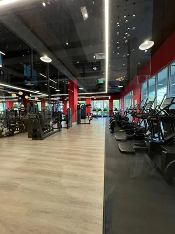 Fitness facility featuring wood-finish flooring, floor-to-ceiling windows, linear LED lighting, and a high-gloss black ceiling