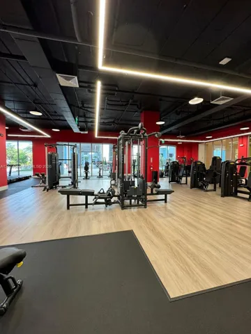 Fitness facility featuring wood-finish flooring, exposed black-painted ceilings, integrated linear LED lighting, and floor-to-ceiling glass windows