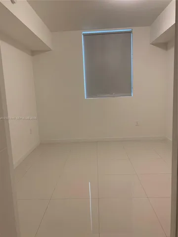 Neutral interior space featuring polished tile flooring, crisp white walls, and a recessed window with a pull-down roller shade