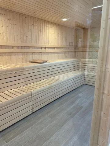 Sauna featuring light-toned wood wall paneling, tiered wood-slat bench seating, recessed lighting, and wood-finish tile flooring