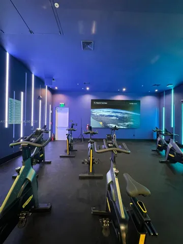 Fitness room featuring integrated wall-mounted vertical LED accent lighting, wall-mounted display screen, and rubberized flooring