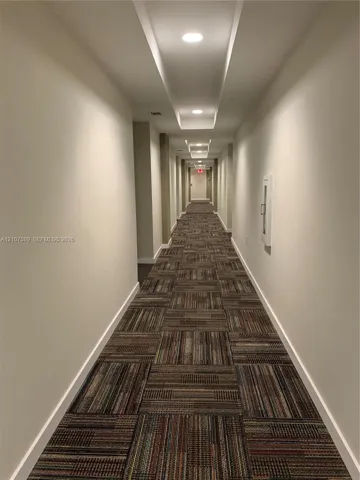 Hallway featuring recessed ceiling lighting, a dropped ceiling architectural detail, and patterned carpet flooring