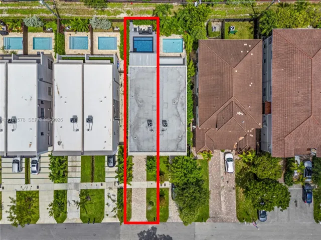 Aerial perspective featuring a paved driveway, a flat roofline, and a rear swimming pool with a stone-surfaced patio