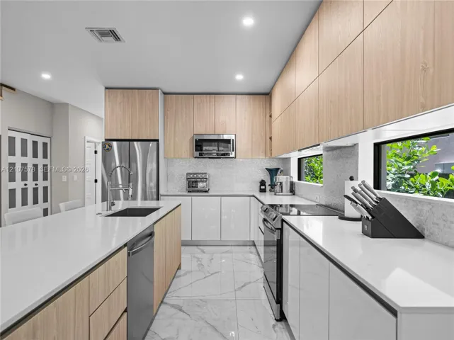 Kitchen featuring white quartz countertops, wood-finish flat-panel cabinetry, stainless steel appliances, marble-patterned flooring, and a horizontal backsplash window