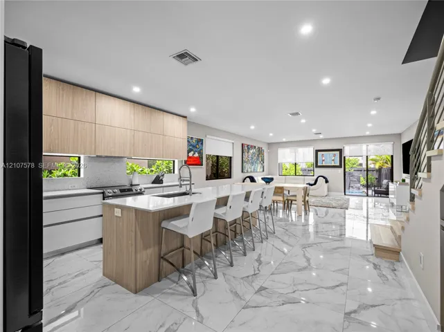 Kitchen featuring two-tone cabinetry with wood-finish upper cabinets, large waterfall-edge island with countertop seating, stone-finish flooring, and recessed lighting