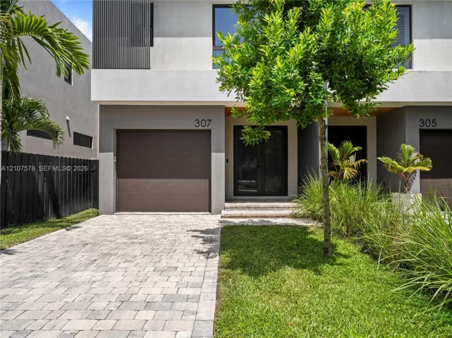 Modern two-story exterior featuring a paver driveway, an attached garage, glass-paneled entry doors, and professional landscaping