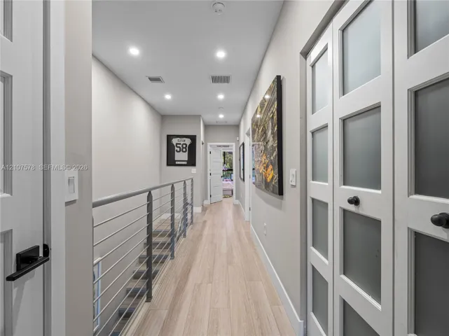Hallway featuring wood-finish flooring, recessed lighting, double doors with frosted glass panels, and a metal horizontal-bar railing