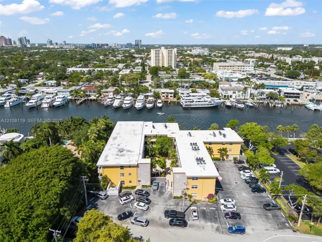 Aerial perspective of a multi-story building featuring a paved surface parking lot, exterior stucco finish, flat roofing, and proximity to a waterway with boat slips