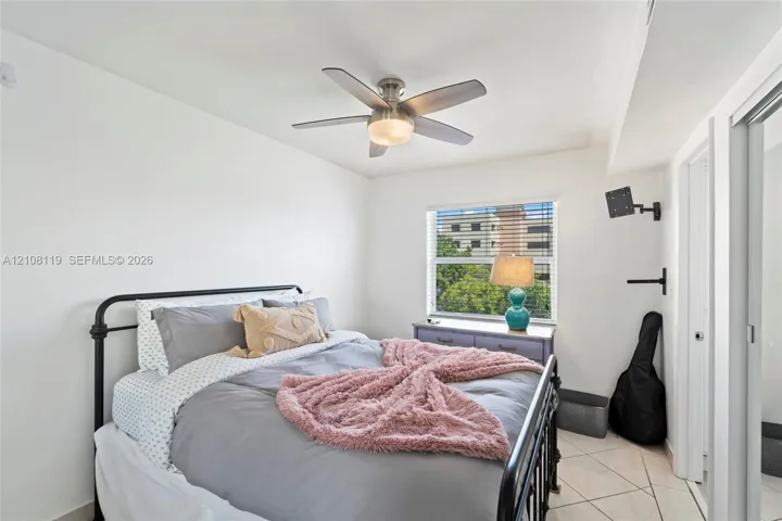 Neutral-toned room featuring a multi-blade ceiling fan with integrated lighting, diamond-patterned tile flooring, a window with horizontal blinds, and a built-in sliding door closet