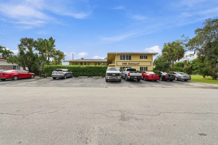 Two-story multi-unit structure featuring a paved surface parking lot, recessed walkways, and mature landscaping