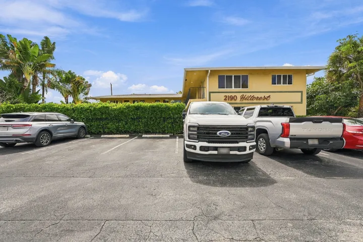 Multi-unit exterior featuring paved surface parking and manicured perimeter hedges