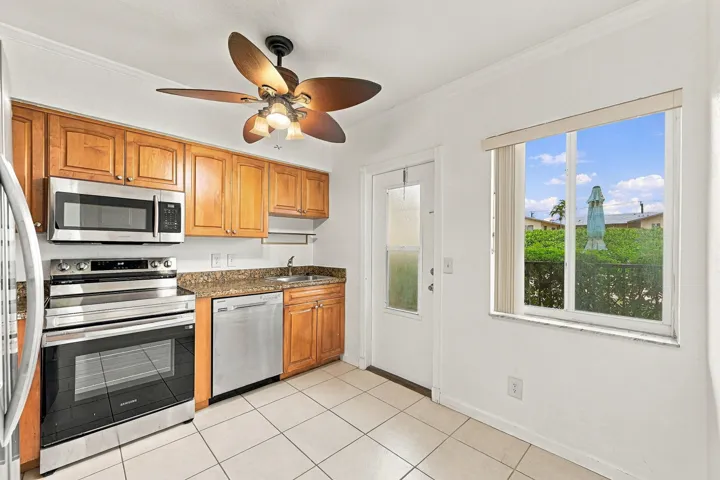 Kitchen featuring wood cabinetry, stone countertops, stainless steel appliances, a ceiling fan, and tile flooring