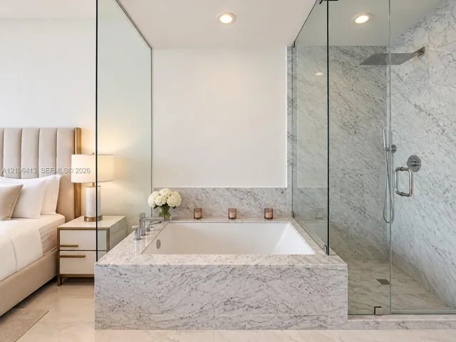 Soaking tub with stone surround, glass-enclosed walk-in shower with rain showerhead, and recessed lighting