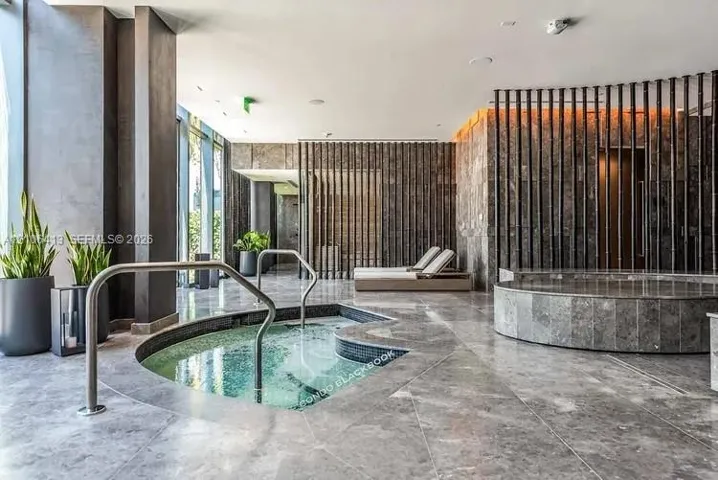 Indoor spa area featuring a built-in jetted tub with stainless steel handrails, circular cold plunge, floor-to-ceiling stone wall cladding, and vertical slat partitions