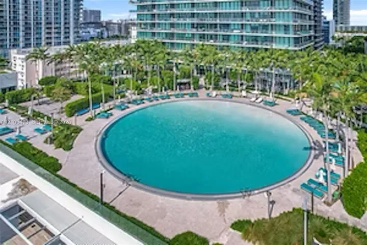 Circular swimming pool with a zero-entry edge, paved pool deck, and mature palm tree landscaping