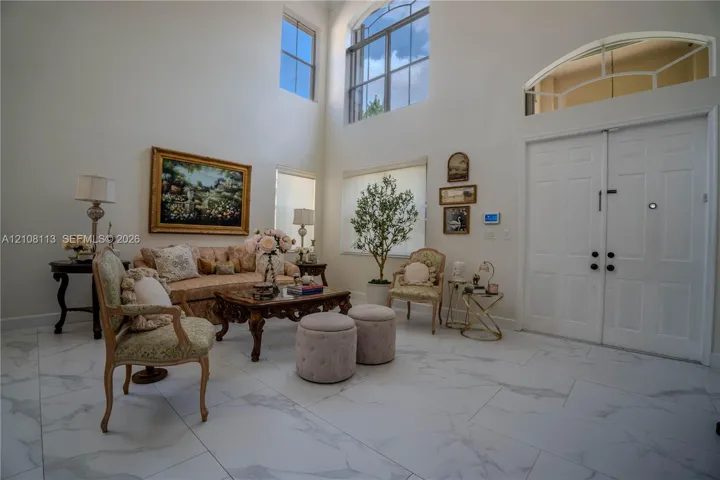 Double-height ceilings featuring expansive windows with an arched transom, double-door entry, and large-format tile flooring with marble-pattern veining