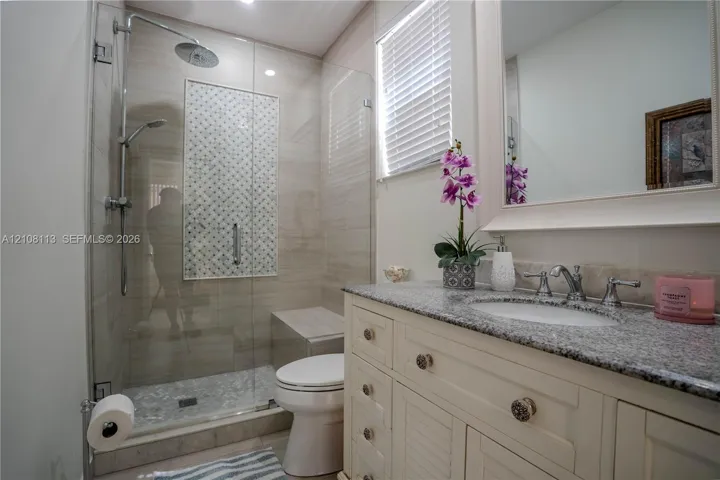 Bathroom featuring a vanity with stone-finish countertop, undermount sink, walk-in glass-enclosed shower with tiled accent inlay, and built-in shower bench