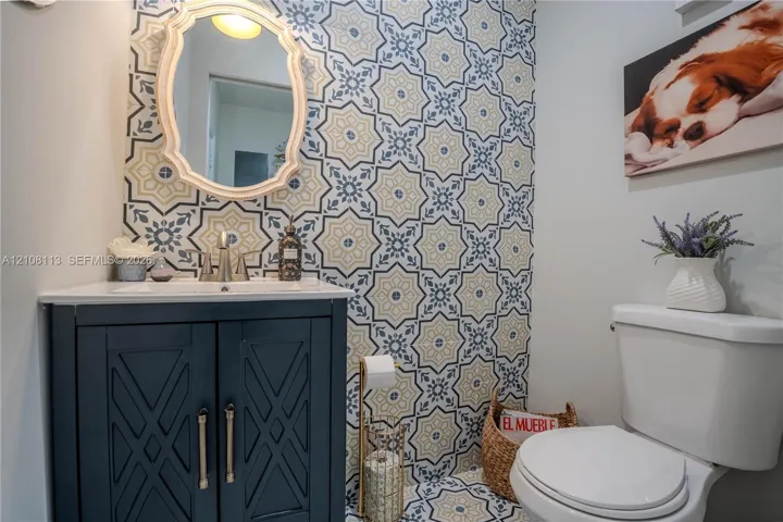 Powder room featuring geometric patterned tile wall and floor accents, navy blue built-in vanity, white countertop with integrated sink, and an arched wall-mounted mirror