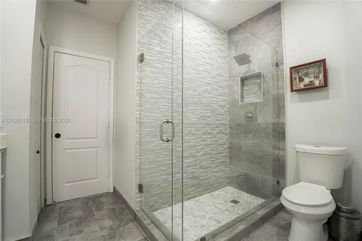 Walk-in shower featuring a frameless glass enclosure, stacked stone accent wall, inset wall niche, and hexagon tile floor