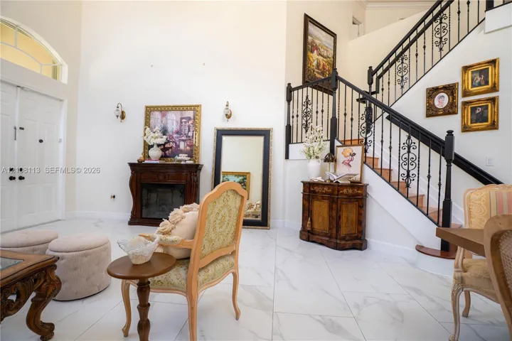 Grand entry featuring double front doors, vaulted ceilings, light-toned stone-finish tile flooring, a staircase with decorative wrought-iron railings, and an integrated dark wood-finish fireplace