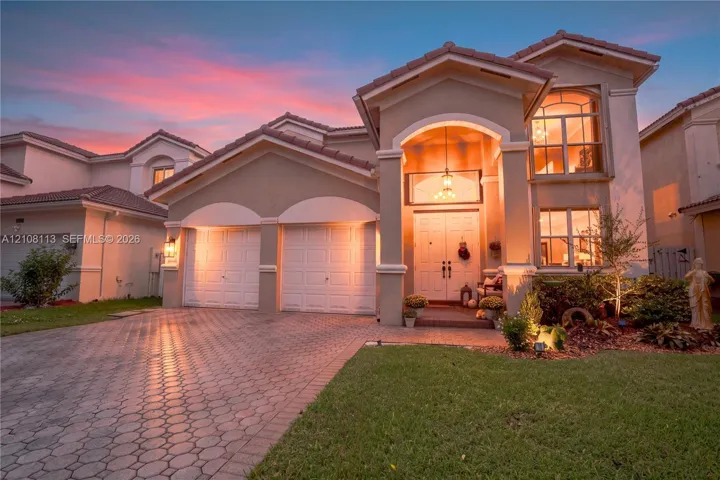 Stucco exterior featuring a dual-car garage, arched covered entryway, paver driveway, and tiled roof