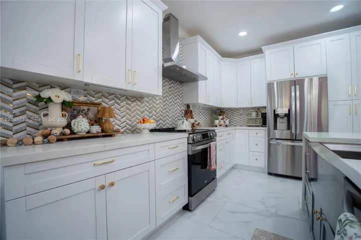 Kitchen featuring white shaker-style cabinetry, herringbone-patterned tile backsplash, stainless steel appliances, and large-format tile flooring