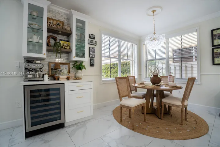 Breakfast area featuring white cabinetry with glass-front uppers, built-in wine refrigerator, white subway tile backsplash, crown molding, and large windows with horizontal blinds