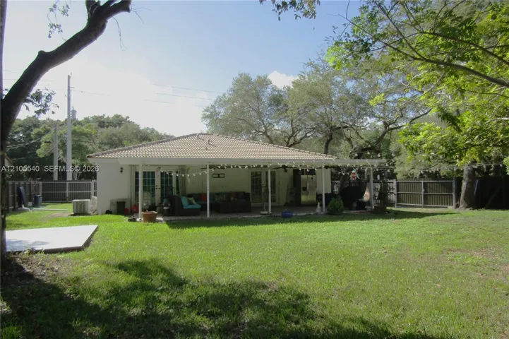 Expansive grass lawn with mature trees, a tile roof, and a covered back patio with support columns
