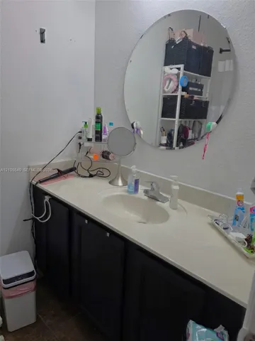 Single vanity with integrated sink, dark wood-finish cabinetry, and a circular wall-mounted mirror