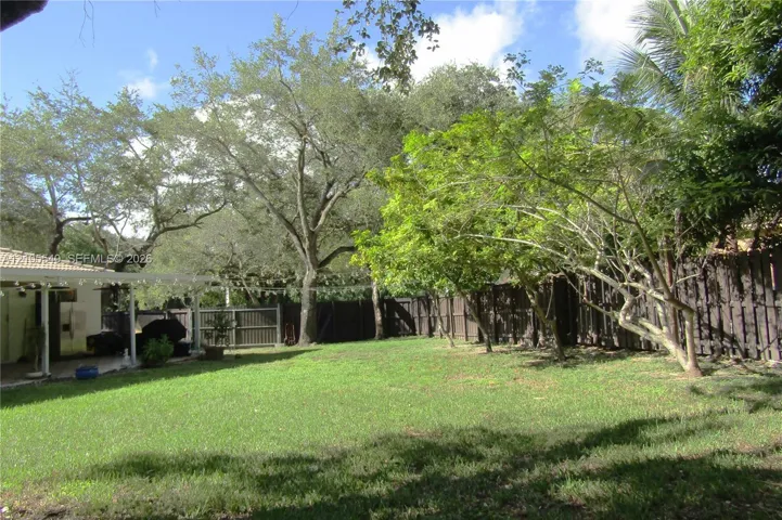 Spacious backyard featuring a manicured lawn, established trees, and a privacy fence