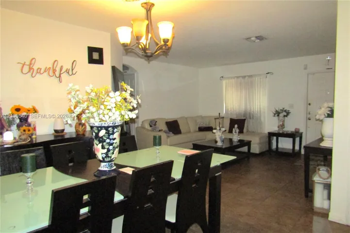 Open concept living and dining areas featuring dark wood-finish flooring, a decorative archway, and a chandelier light fixture
