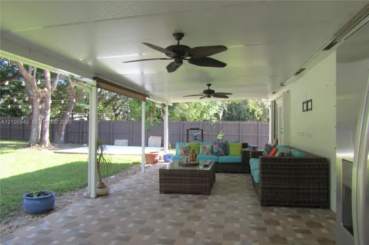 Expansive covered patio featuring a tiled floor, dual ceiling fans, and a solid perimeter fence