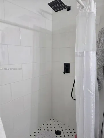 Shower with white subway tile, a matte black shower head, and a black and white mosaic tile floor