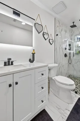 Bathroom featuring a white shaker-style vanity with stone-composite countertop, matte black hardware, integrated LED-backlit mirror, and glass-enclosed shower with large-format wall tile and geometric-patterned flooring
