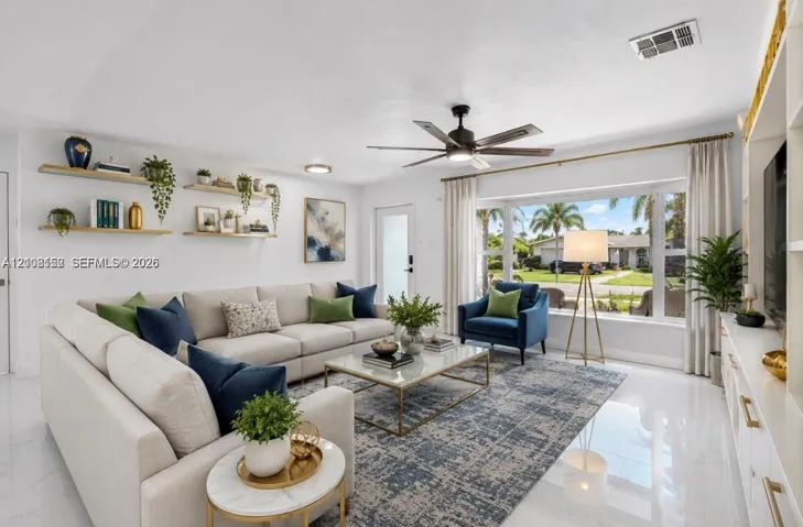 Living area featuring a large bay window, light-toned tile flooring, custom built-in cabinetry, floating wall shelves, and a ceiling fan