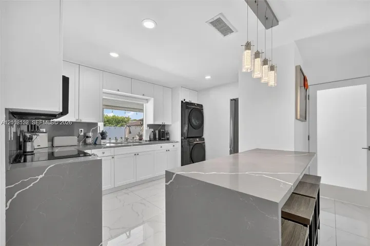 Kitchen featuring white cabinetry, grey stone-finish countertops with a waterfall edge, recessed lighting, multi-pendant fixture, and white tile flooring