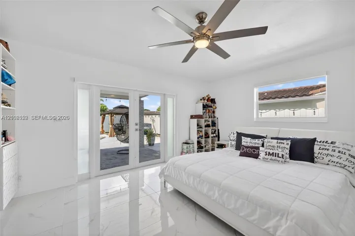 Glossy white tile flooring, ceiling fan with integrated lighting, built-in shelving, and dual glass-panel exterior doors
