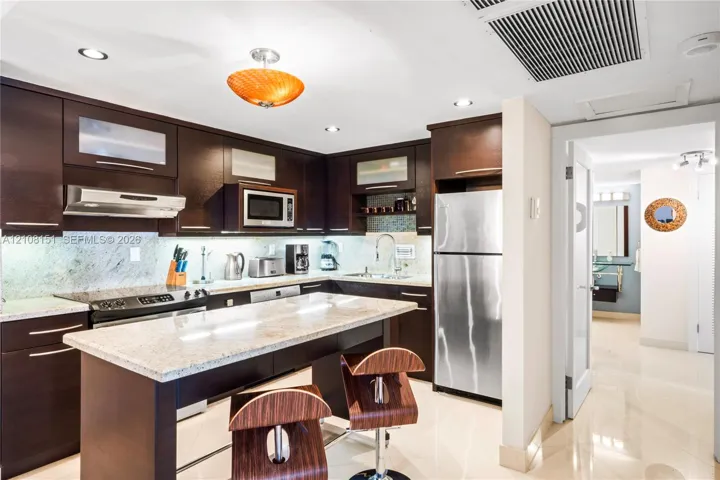 Kitchen featuring dark wood-finish cabinetry, stone countertops, stainless steel appliances, and a central island