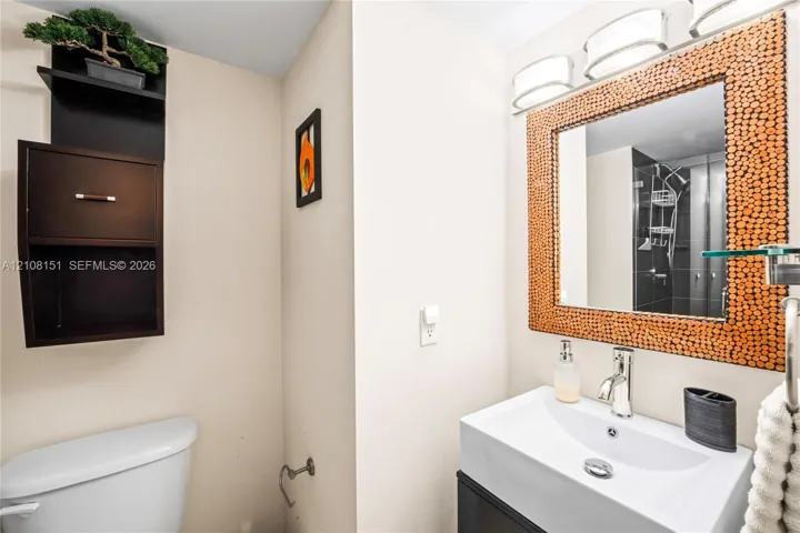 Wall-mounted cabinetry, integrated mirror with textured surround, triple-light vanity fixture, rectangular ceramic sink, and single-lever chrome faucet
