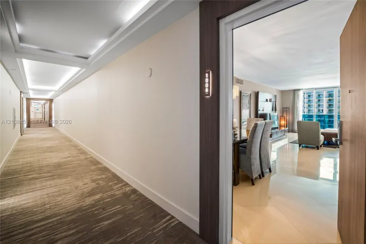 Interior hallway featuring recessed ceiling lighting and patterned carpeting, opening to an entryway with light-colored tile flooring and a wall-mounted unit number plate
