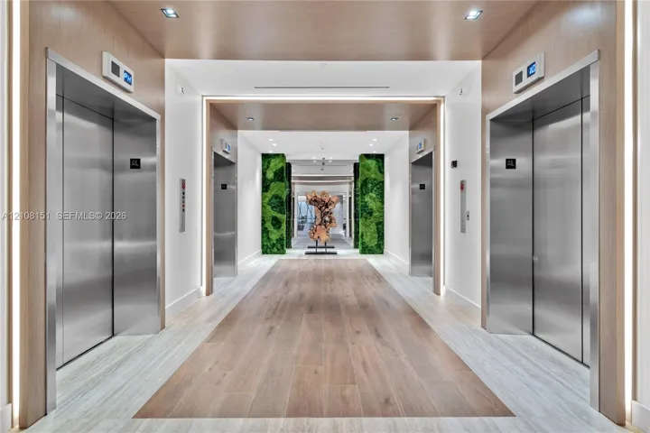 Elevator lobby featuring stainless steel doors, wood-finish wall paneling, integrated LED lighting, and decorative moss-covered columns