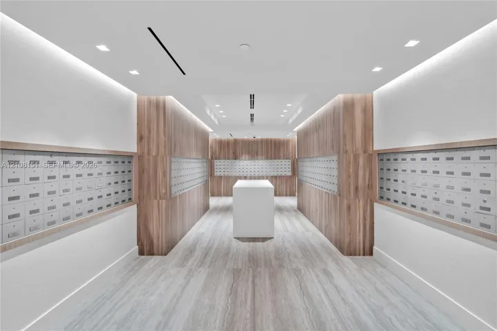 Mail center featuring wood-panel wall accents, recessed lighting, integrated wall-mounted mailboxes, stone-finish flooring, and a central white pedestal