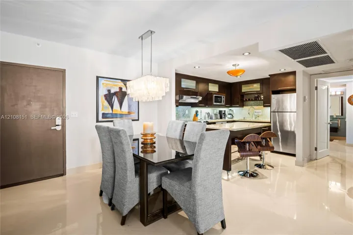 Kitchen area featuring dark cabinetry, stone-finish countertops, stainless steel appliances, polished tile flooring, and a rectangular multi-light pendant fixture