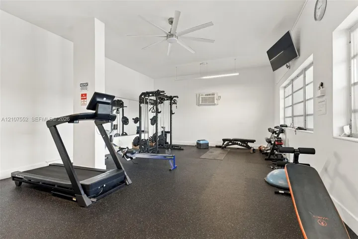 Interior room featuring rubberized flooring, mirrored wall, multi-blade ceiling fan, and large windows