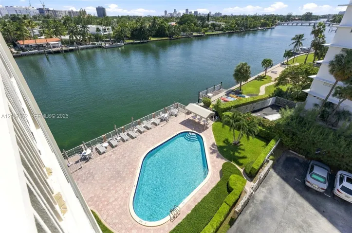 Waterfront swimming pool with paver patio, manicured landscaping, and bulkhead shoreline