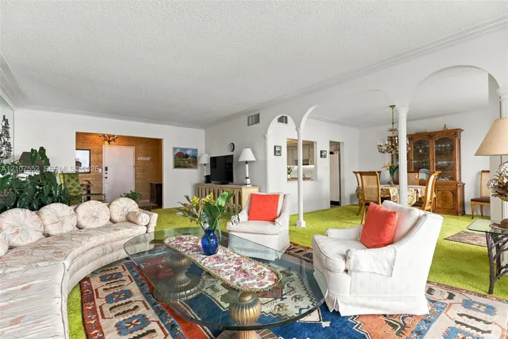 Living area featuring decorative archways with columns, a pass-through window to the kitchen, and a textured ceiling